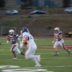 An AAHS football player runs with the ball across the playing field agains a blurred background.
